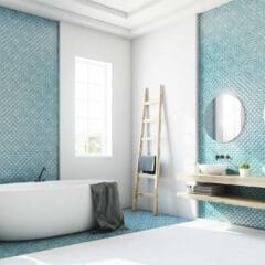 Modern bathroom with a freestanding tub, ladder towel rack, dual sinks with round mirrors, and blue patterned tile accent walls. Sunlight streams through tall windows.