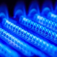 Close-up of blue flames from a natural gas burner, showing multiple rows with bright blue, evenly spaced flames in a dark background.